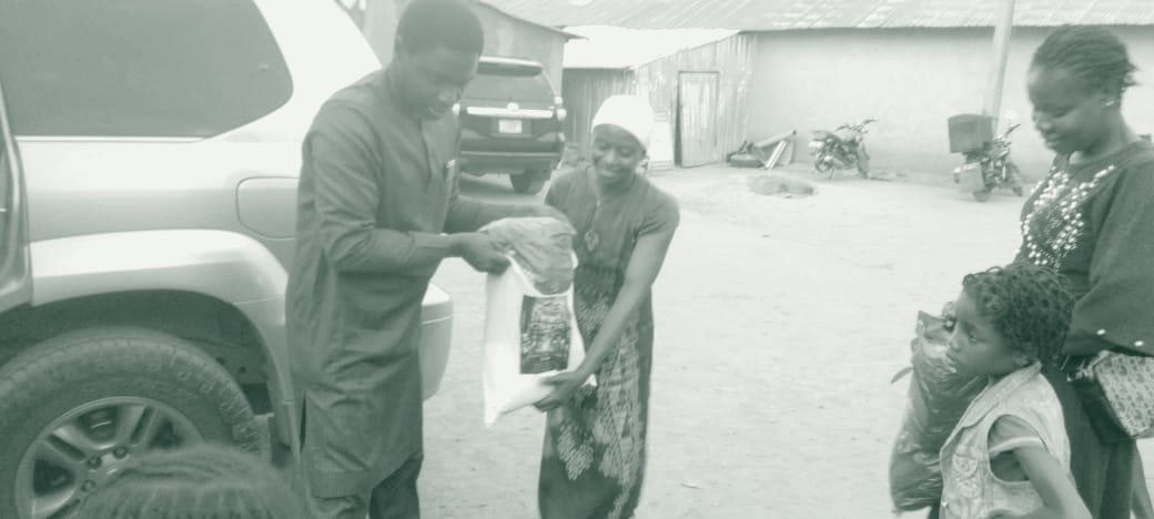 A Fisho Initiative volunteer hands a food package directly to a mother, with her children looking on.