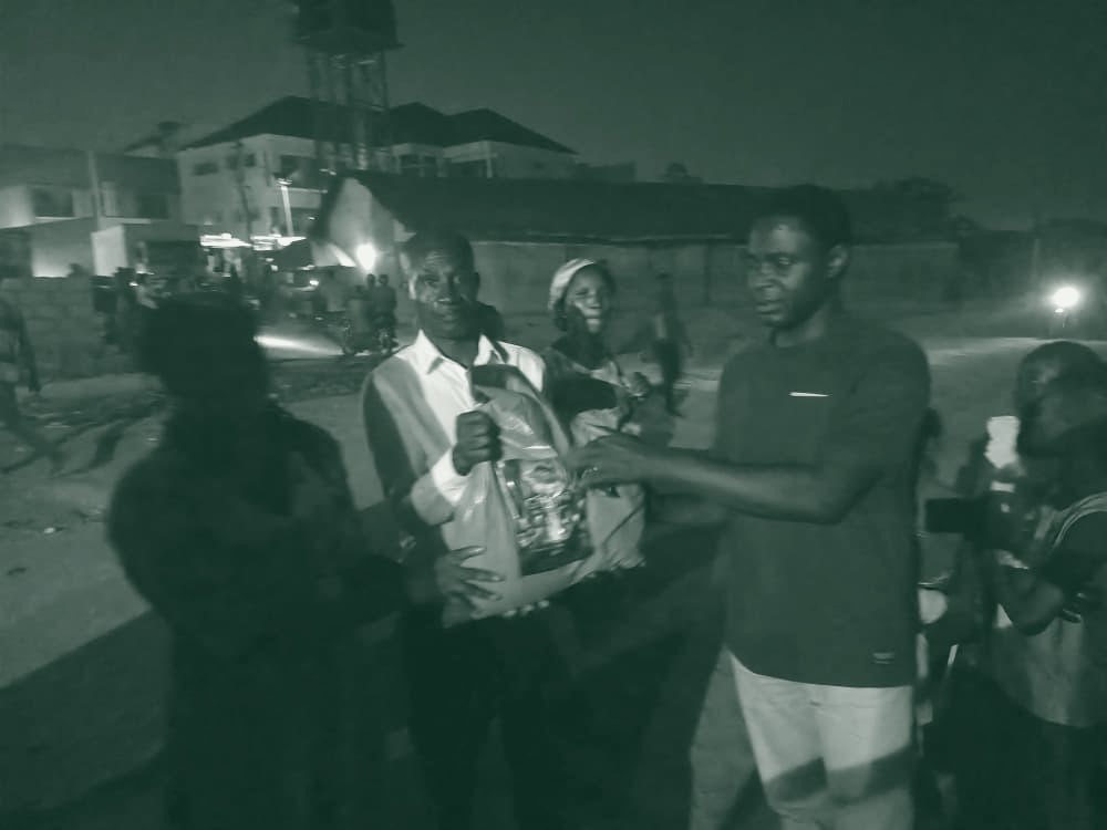 A volunteer hands a food package to a recipient after dark.